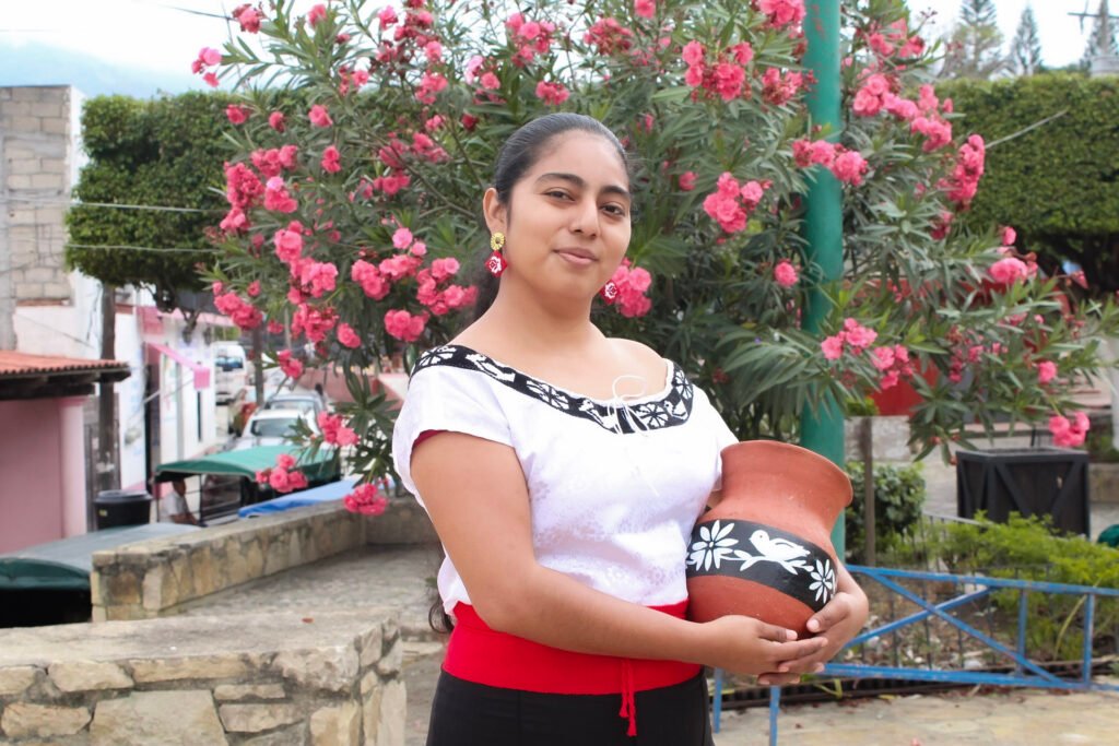mujer sosteniendo su producto elaborado con alfareria y decorado con bordado zoque pintado a mano