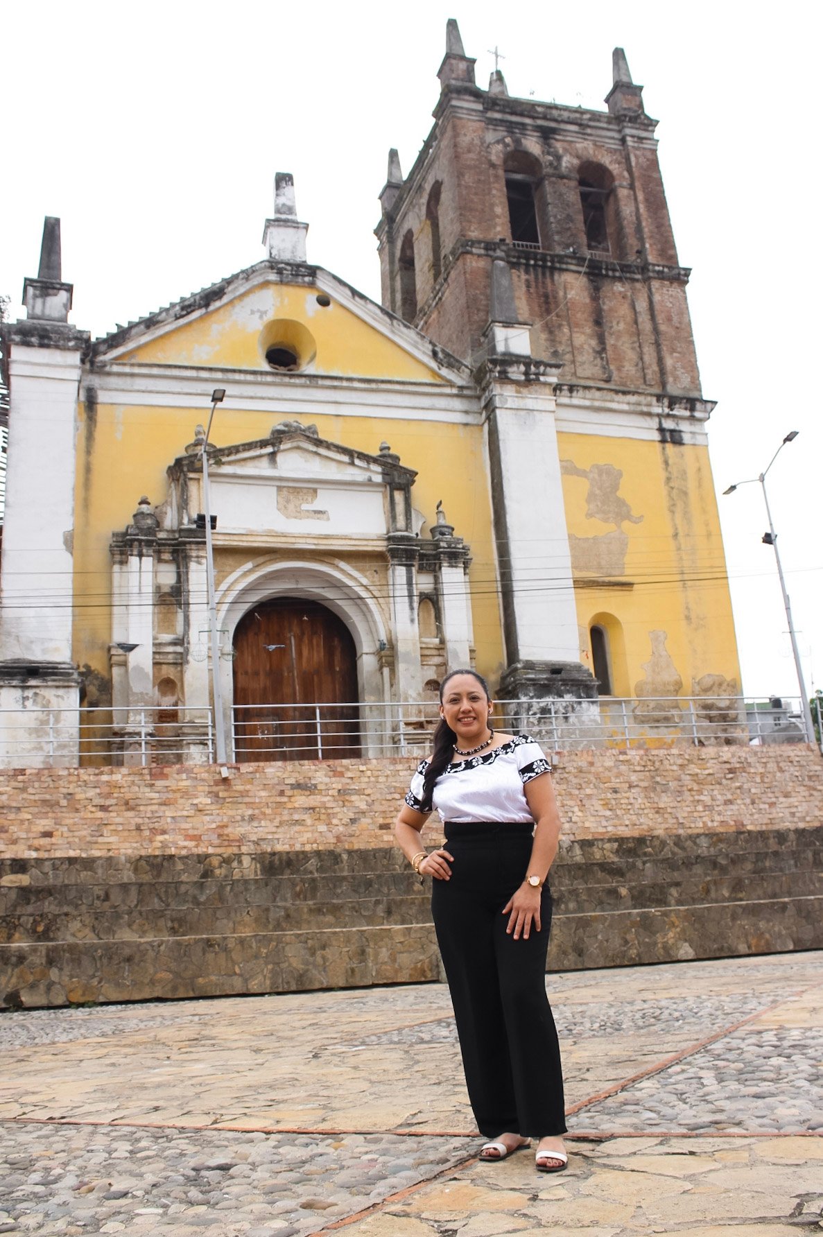 mujer artesana zoque de sunyipa yomo posando con blusa zoque y atras la iglesia de copainala